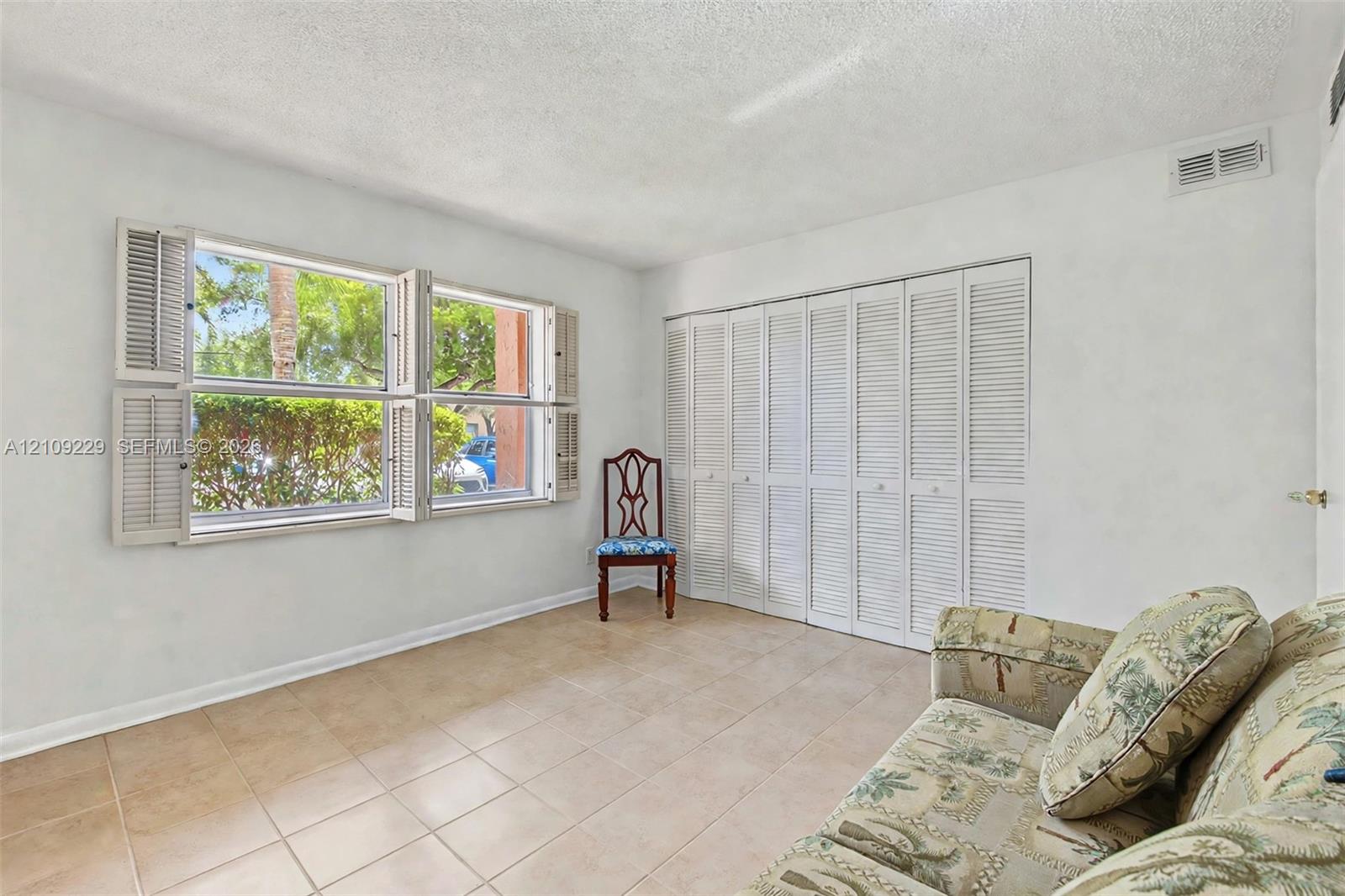 Room featuring tile flooring, white accordion-style closet doors, and windows equipped with louvered shutters