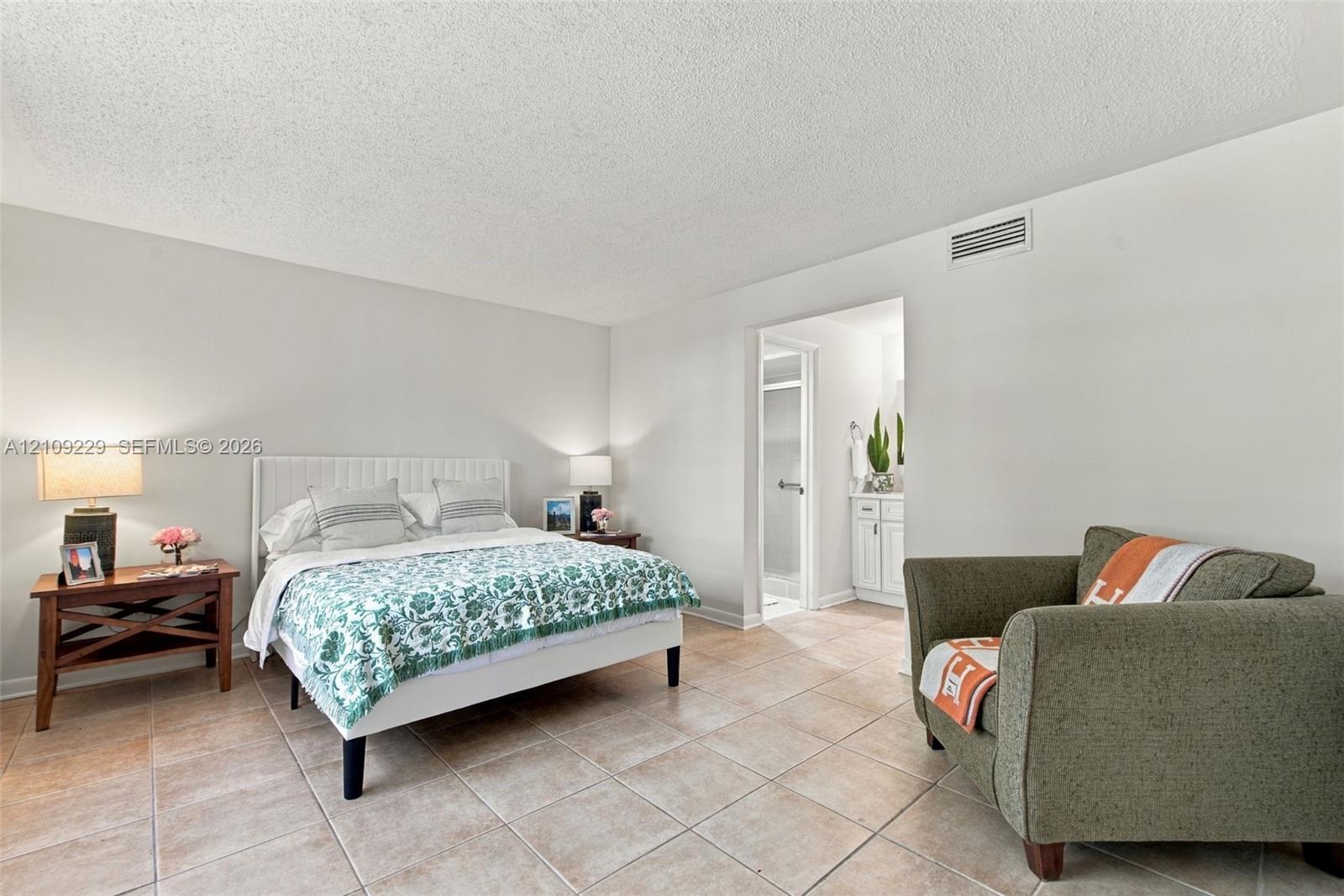 Neutral-toned bedroom with tile flooring and a doorway leading to an additional tiled space with a white vanity cabinet