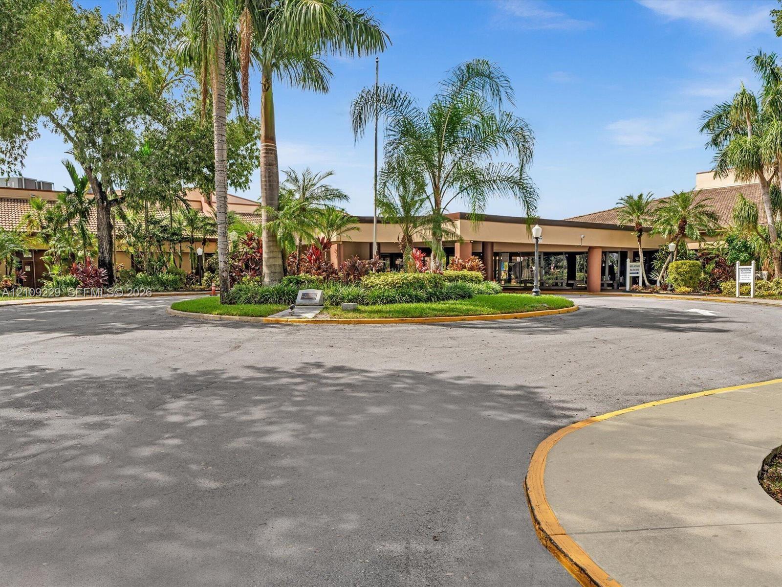 Paved circular drive featuring a central landscaped island with mature palm trees and established tropical foliage