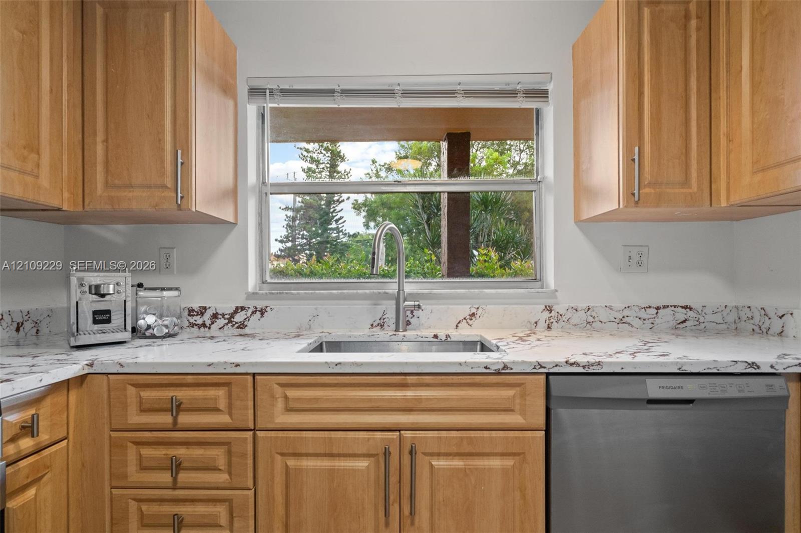 Kitchen featuring natural-finish wood cabinetry, patterned stone-surface countertops, a stainless steel undermount sink with a pull-down faucet, and a stainless steel dishwasher