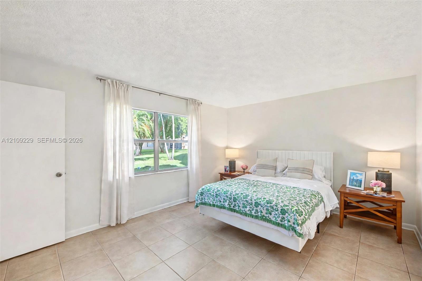 Neutral interior featuring tile flooring, textured ceiling, and a single-pane window with exterior greenery
