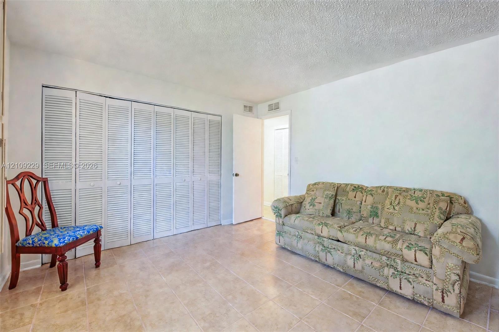 Spacious room featuring neutral tile flooring, expansive wall-to-wall closets with white louvered doors, and a solid-core interior door