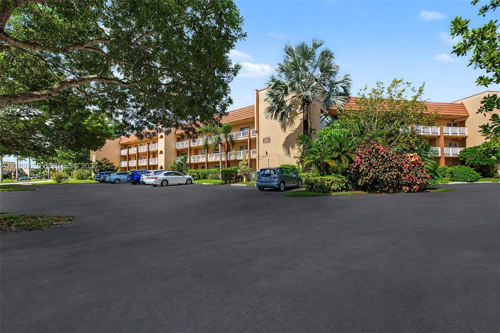 Multi-story building exterior featuring a neutral stucco facade, tiered balconies with white railings, and mature tropical landscaping Multi-story building exterior featuring a neutral stucco facade, tiered balconies with white railings, and mature tropical landscaping