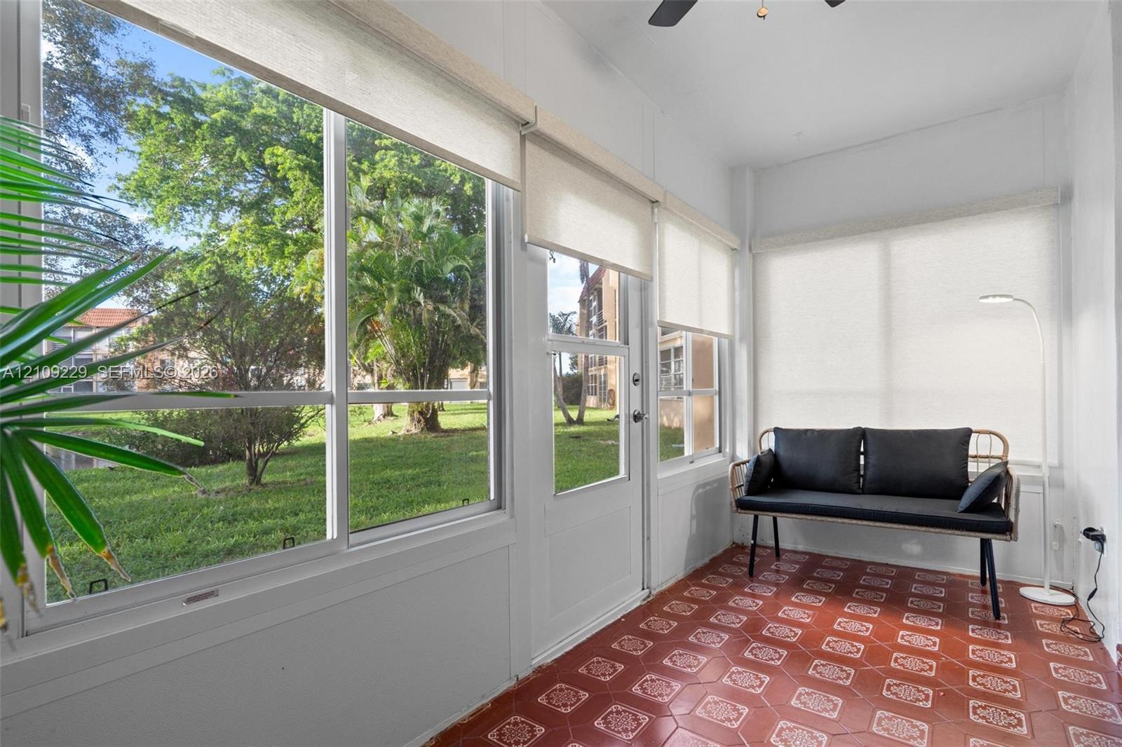 Enclosed sunroom featuring expansive windows with fitted roller shades, terra cotta-style tile flooring, and a ceiling fan