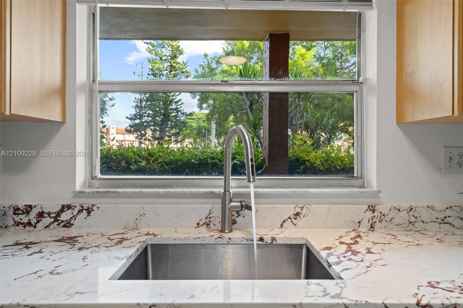 Stainless steel under-mount sink featuring a high-arc pull-down faucet, stone-finish countertops with integrated backsplash, and light-tone wood-finish cabinetry