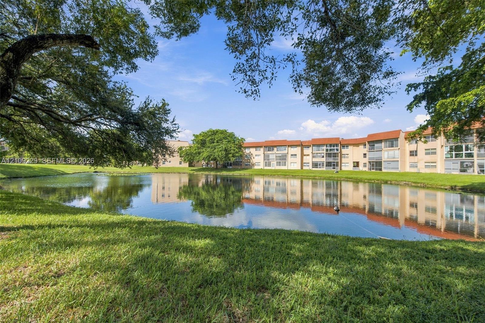 Exterior grounds featuring a pond, mature canopy trees, and grass landscaping with multi-story residential architecture