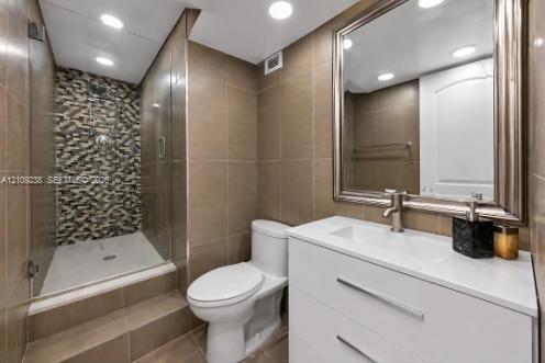 Modern bathroom featuring a walk-in glass-enclosed shower with mosaic stone accent tile, white vanity cabinet with an integrated sink, sleek chrome fixtures, and neutral oversized wall tile