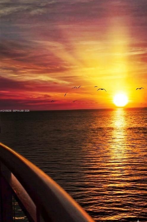 Coastal balcony featuring a structural railing overlooking a sunset over the ocean