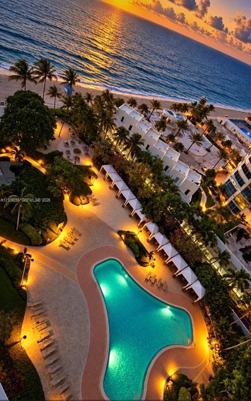Aerial perspective of coastal property featuring an expansive swimming pool with hardscaped surround, multiple cabanas, mature palm trees, and direct oceanfront access