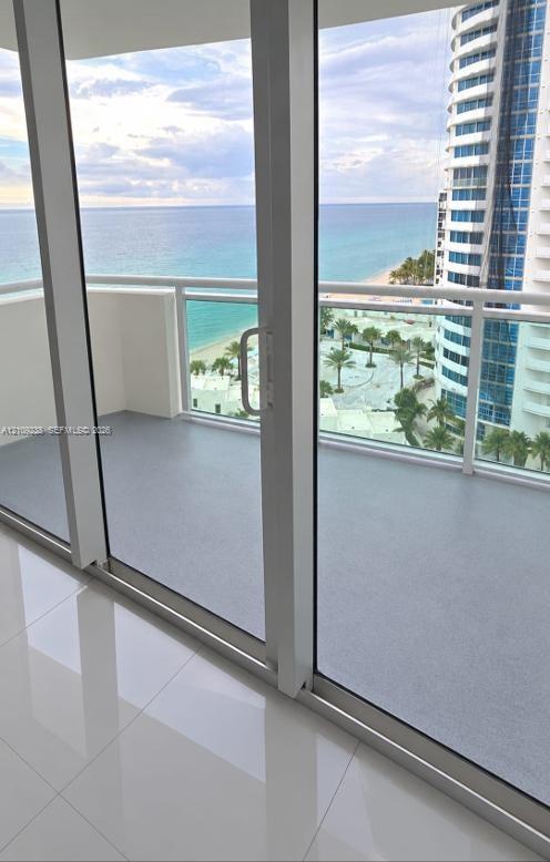 Floor-to-ceiling glass sliding doors opening to a private balcony with a white metal railing, finished with high-gloss tile flooring
