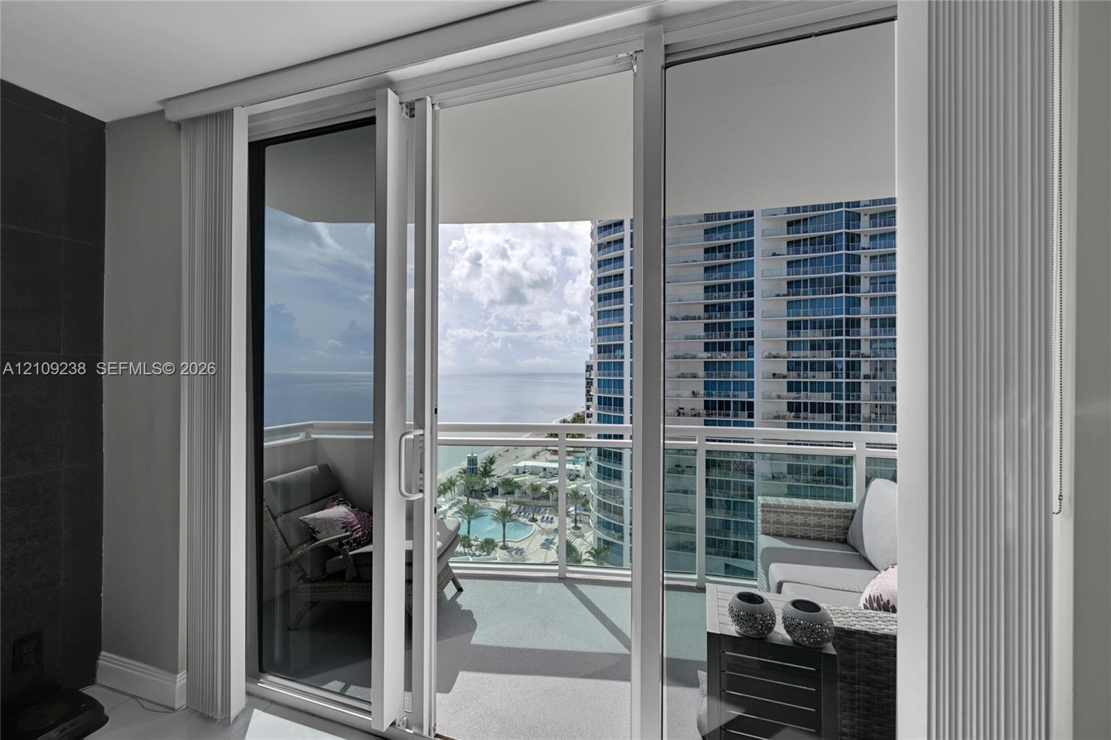 Floor-to-ceiling sliding glass door system, balcony with white metal railing, and ocean horizon backdrop