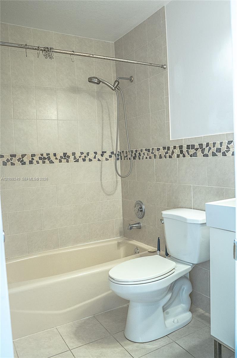 Full bathtub with integrated showerhead, neutral ceramic wall tile, decorative mosaic tile inlay, and floor tiling