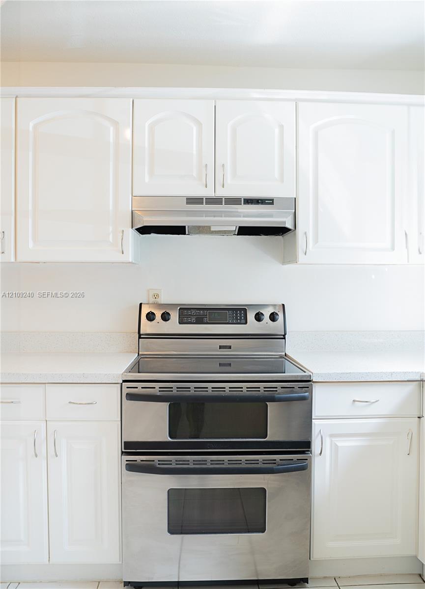 White cabinetry featuring arched-panel doors, stainless steel double-oven range, integrated stainless steel range hood, and solid-surface countertops