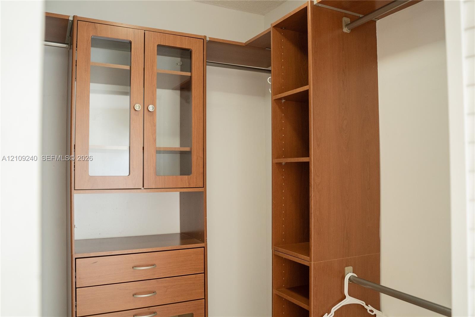 Custom wood-finish closet storage system featuring built-in cabinetry, glass-front upper doors, three drawers with metallic pulls, adjustable shelving, and integrated garment rods