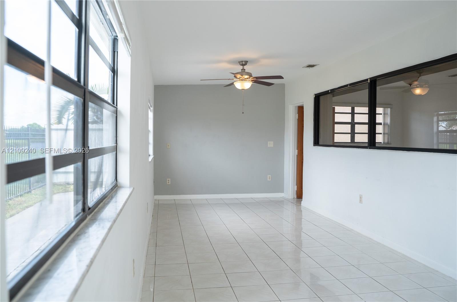 Ceramic tile flooring, expansive multi-pane windows, interior horizontal window pass-through with dark trim, and a ceiling-mounted light fixture with fan