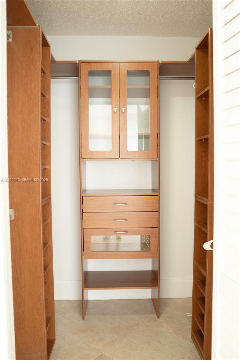 Custom built-in wood-finish cabinetry featuring glass-panel cabinet doors, three integrated drawers, open shelving, and hanging rods
