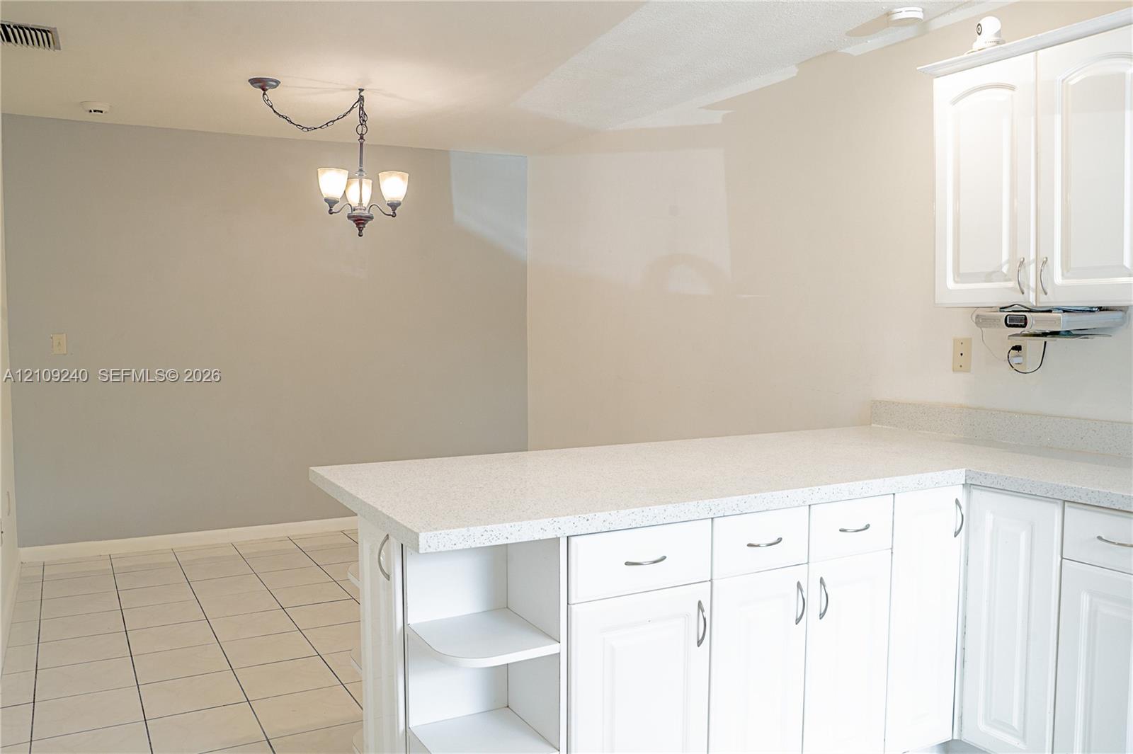 White cabinetry with integrated shelving, stone-finish countertops, tile flooring, and a multi-light chandelier