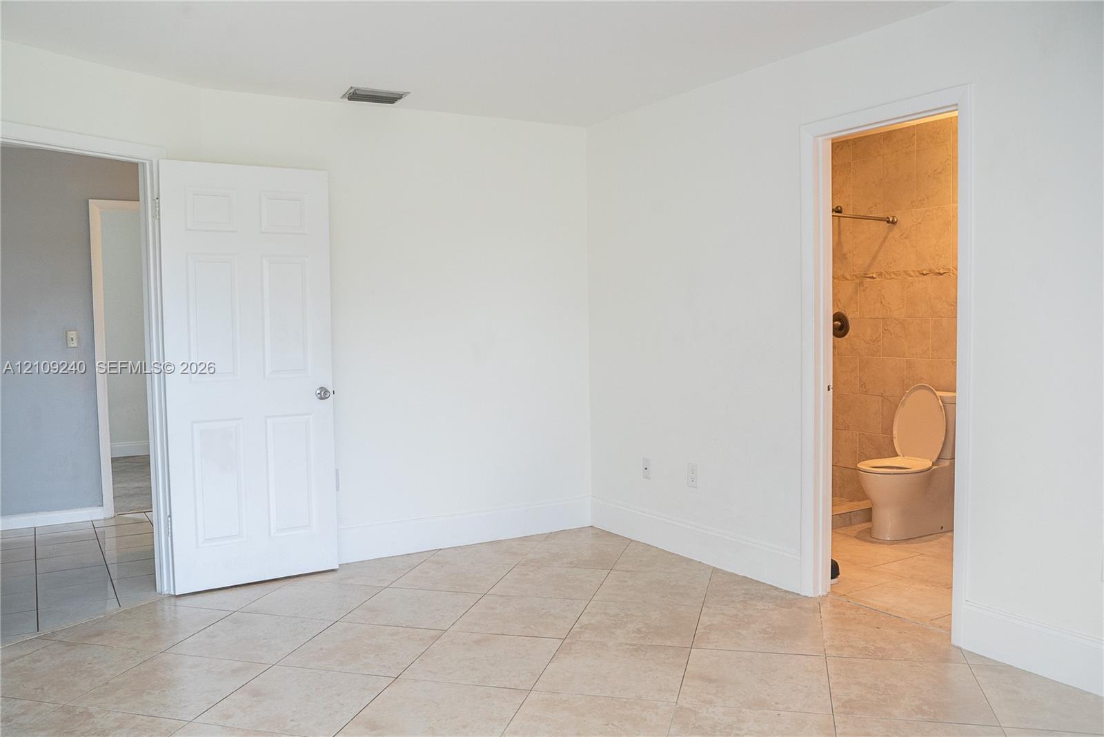 Interior space featuring neutral tile flooring, white-paneled interior doors, and a bathroom containing a tiled shower enclosure and ceramic toilet