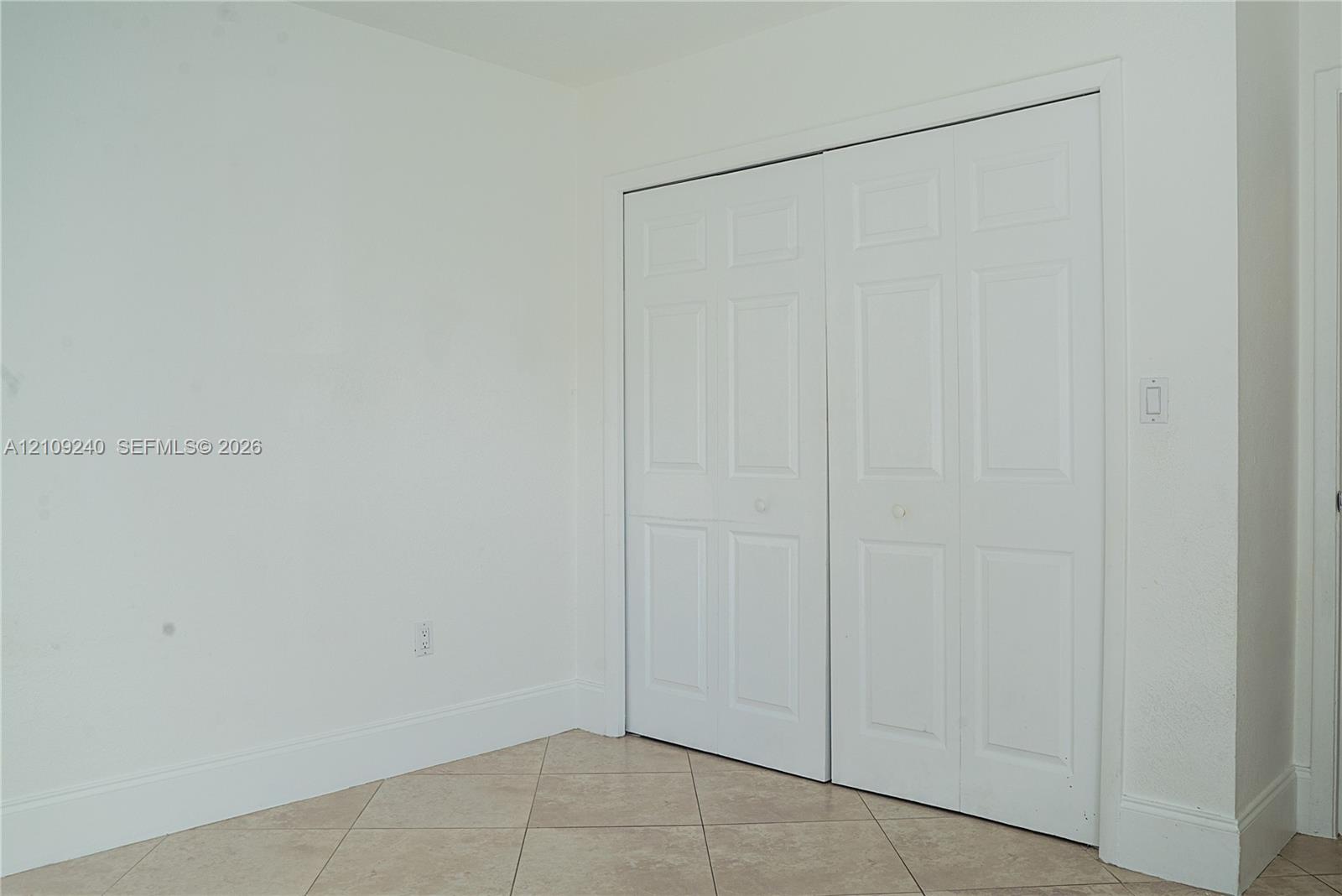 Neutral-toned interior space featuring light-colored tile flooring and dual-panel closet doors