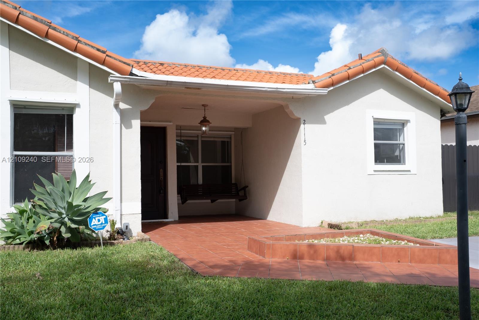 Stucco exterior featuring a clay tile roof, covered front porch with tiled flooring, and a raised exterior planter