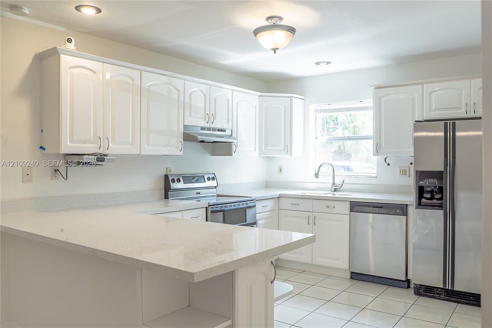 Kitchen featuring white cabinetry, solid-surface countertops with a breakfast bar, stainless steel appliances, and tile flooring