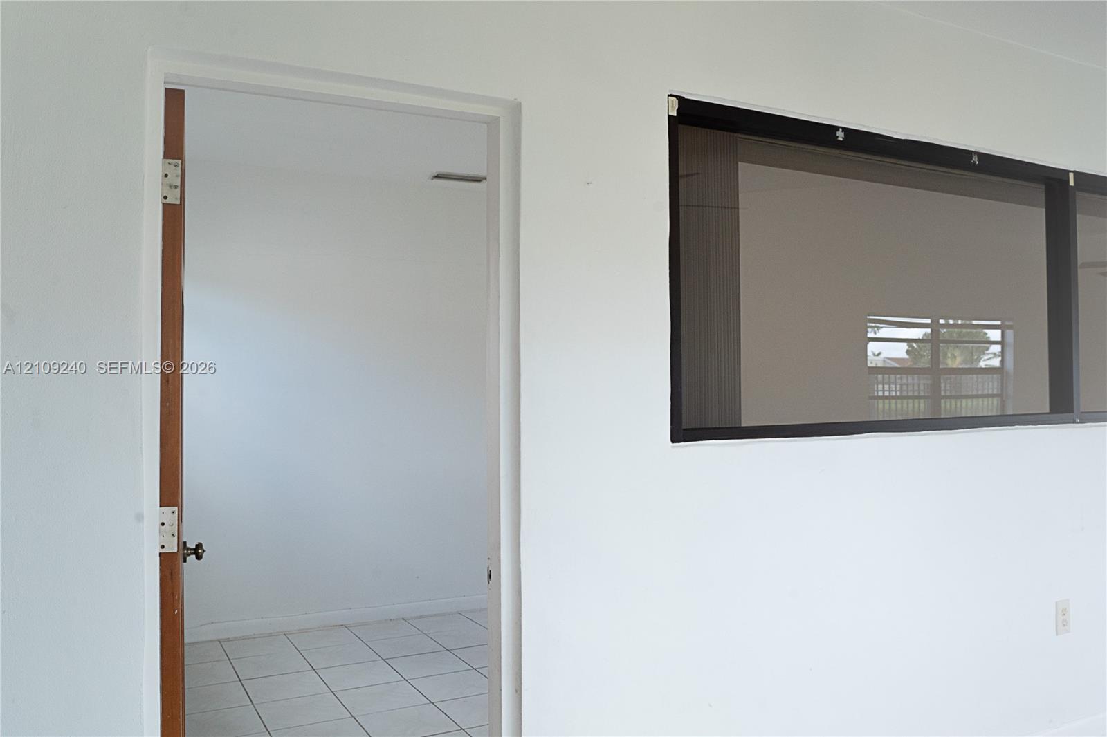 Interior space featuring light-colored tile flooring, a solid wood-finish door, and a horizontal window with a dark frame