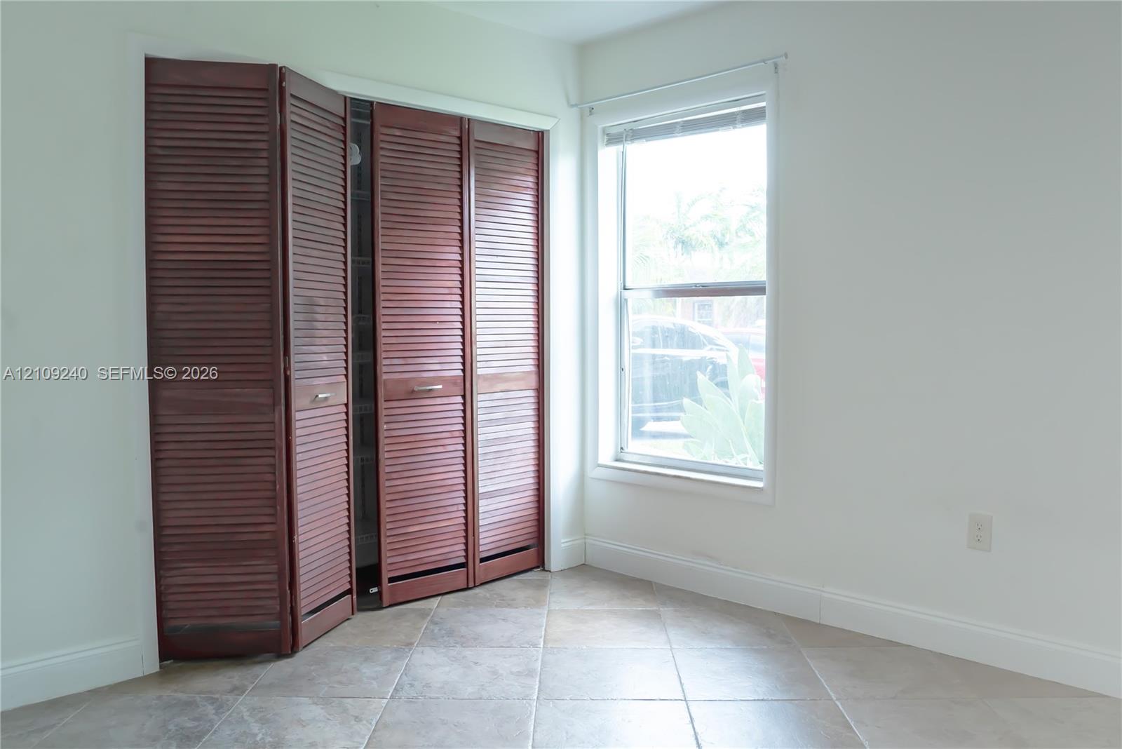 Stained wood louvered bi-fold closet doors and neutral-tone tile flooring