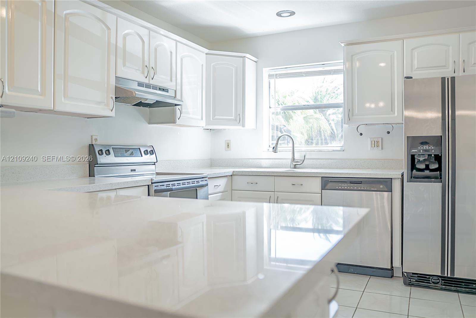 Kitchen featuring white cabinetry, solid-surface countertops, stainless steel appliances, and tile flooring