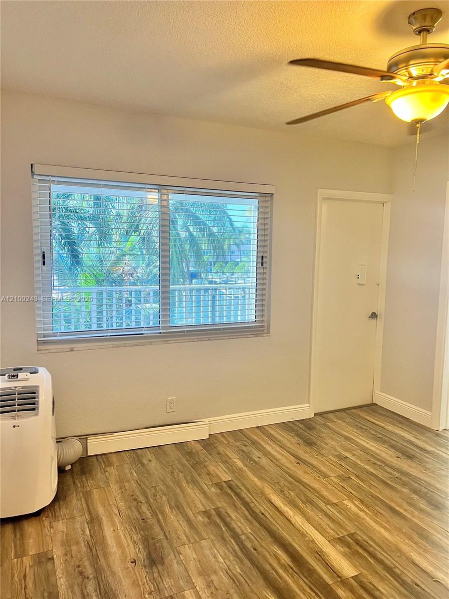 Interior space featuring wood-finish flooring, a ceiling fan with integrated lighting, and a large window equipped with horizontal blinds