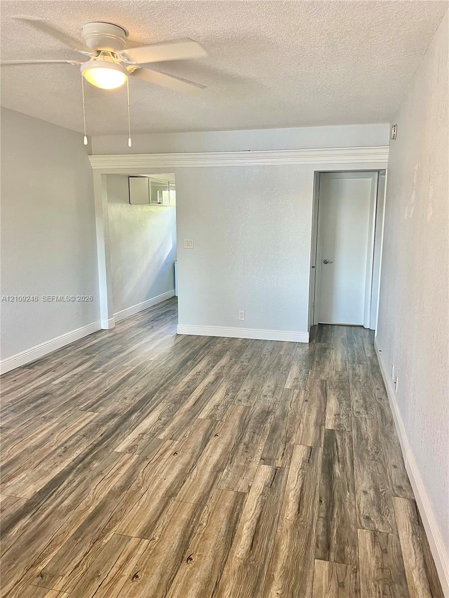 Wood-finish flooring, neutral wall tones, ceiling fan with integrated light fixture, and crown molding