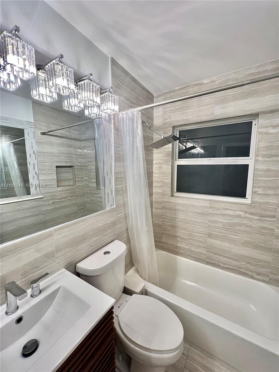 Full-wall neutral stone-look tiling, multi-light glass vanity fixture, integrated shower niche, rectangular vessel sink with chrome faucet, and overhead rainfall shower head