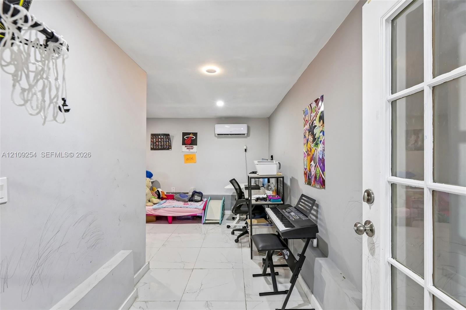 Interior room featuring large-format light-toned tile flooring, recessed lighting, and a wall-mounted ductless air conditioning unit, accessible via a glass-paneled entry door