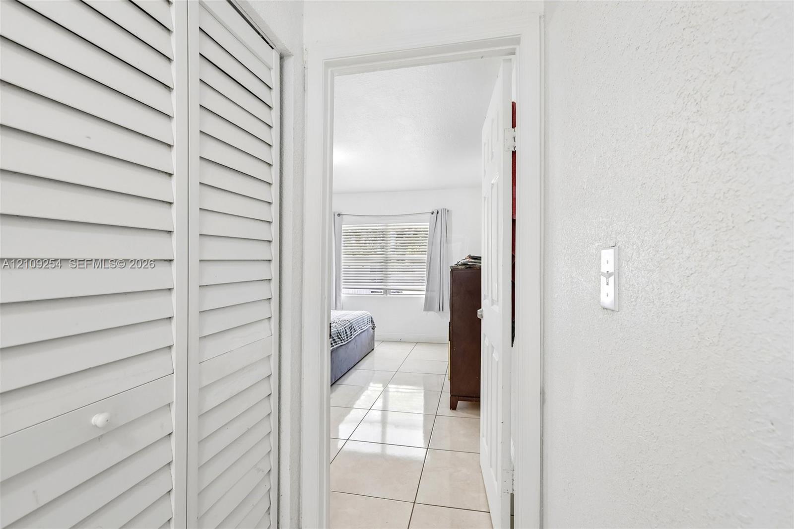 White louvered bi-fold closet doors and neutral large-format tile flooring