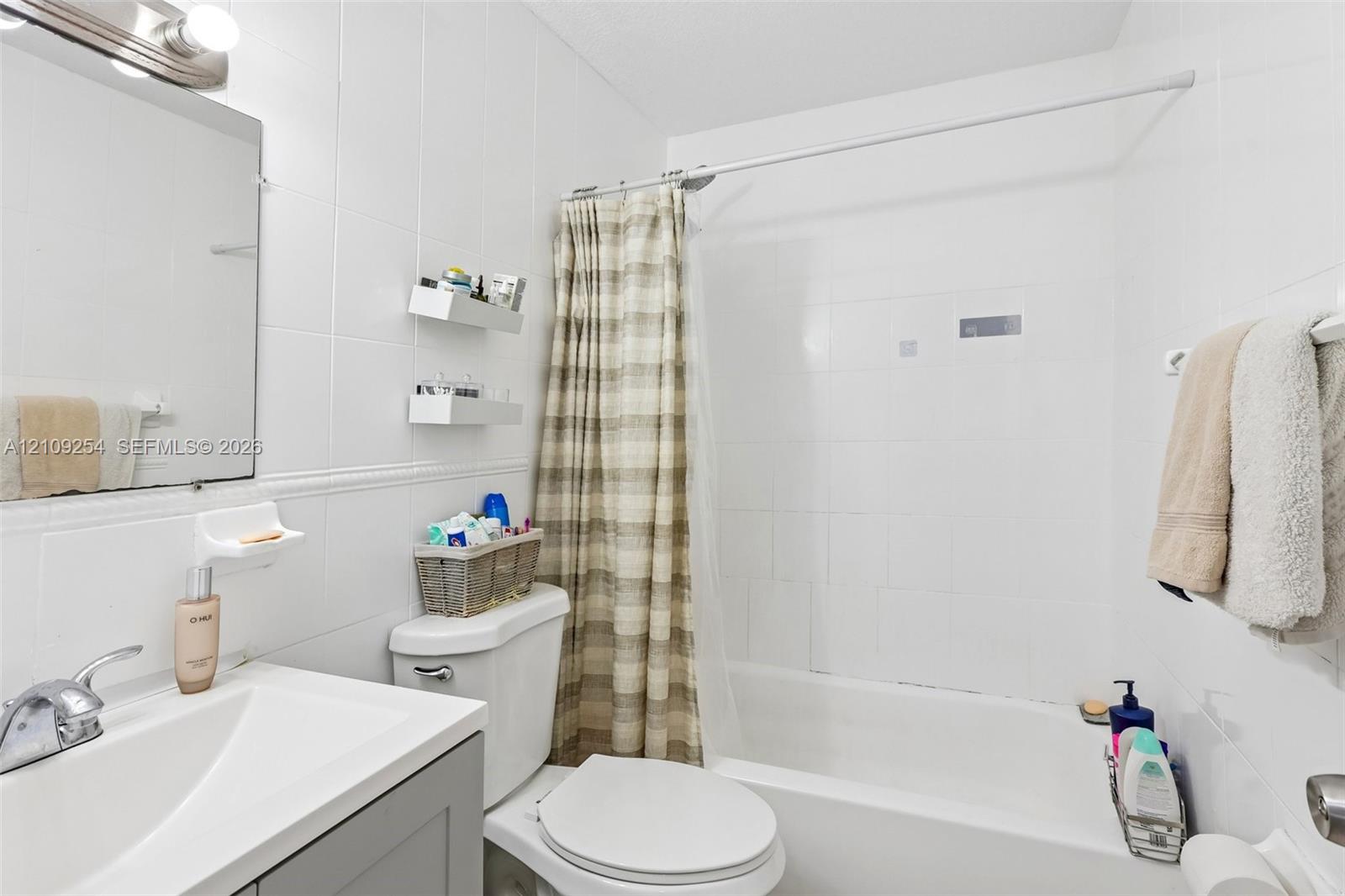 Bathroom featuring a vanity with an integrated sink, polished chrome faucet, white tile wall surround, built-in wall shelving, and a combination tub and shower