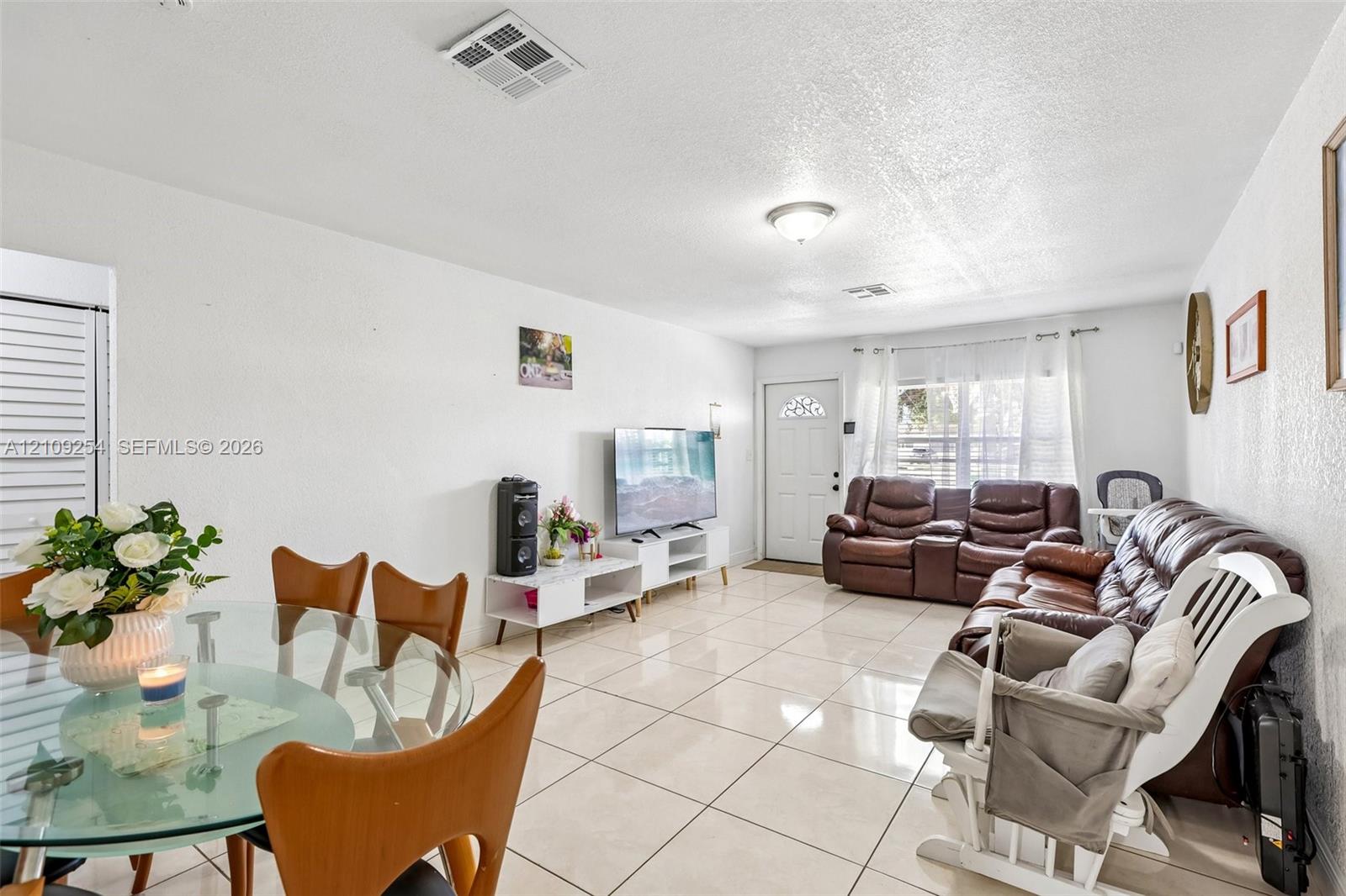 Open floor plan featuring large-format ceramic tile flooring, neutral wall finishes, a flush-mount ceiling light fixture, and a window with white casing Open floor plan featuring large-format ceramic tile flooring, neutral wall finishes, a flush-mount ceiling light fixture, and a window with white casing