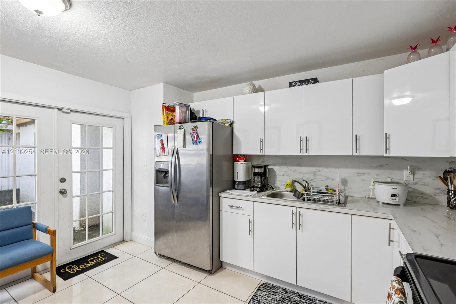 Kitchen featuring white slab-front cabinetry, stone-finish countertops, stainless steel side-by-side refrigerator, tile flooring, and glass-paneled exterior door