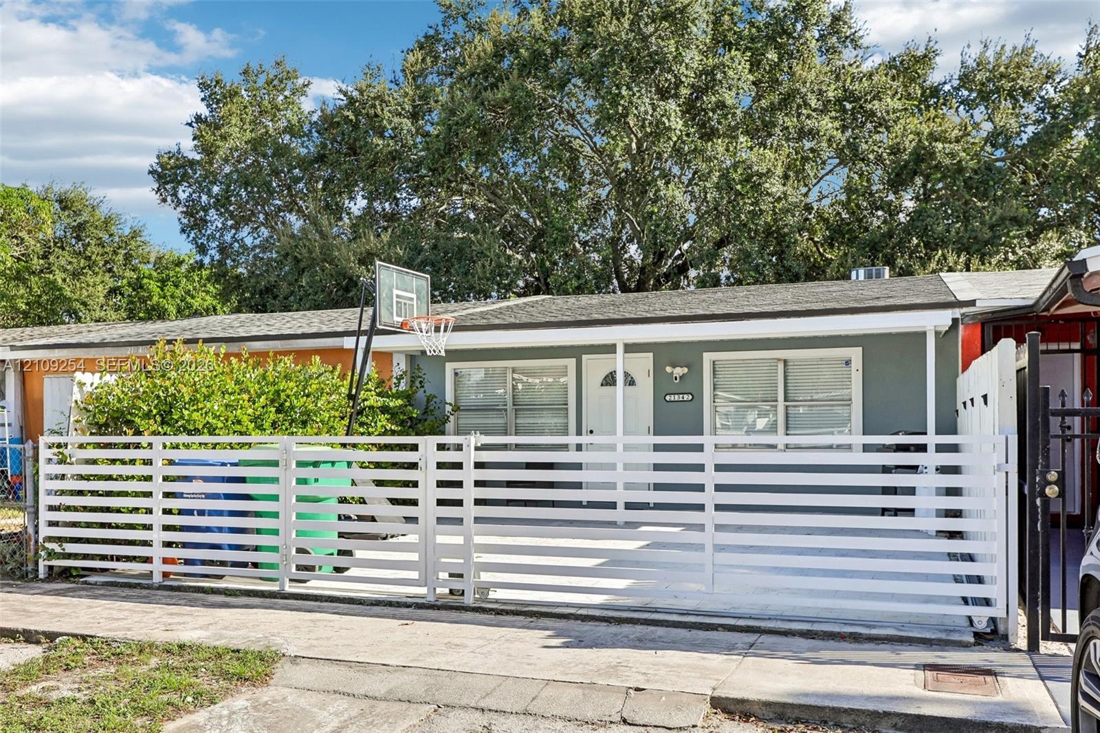 Single-story exterior featuring a horizontal slat privacy fence, concrete paved front area, and mature canopy trees Single-story exterior featuring a horizontal slat privacy fence, concrete paved front area, and mature canopy trees