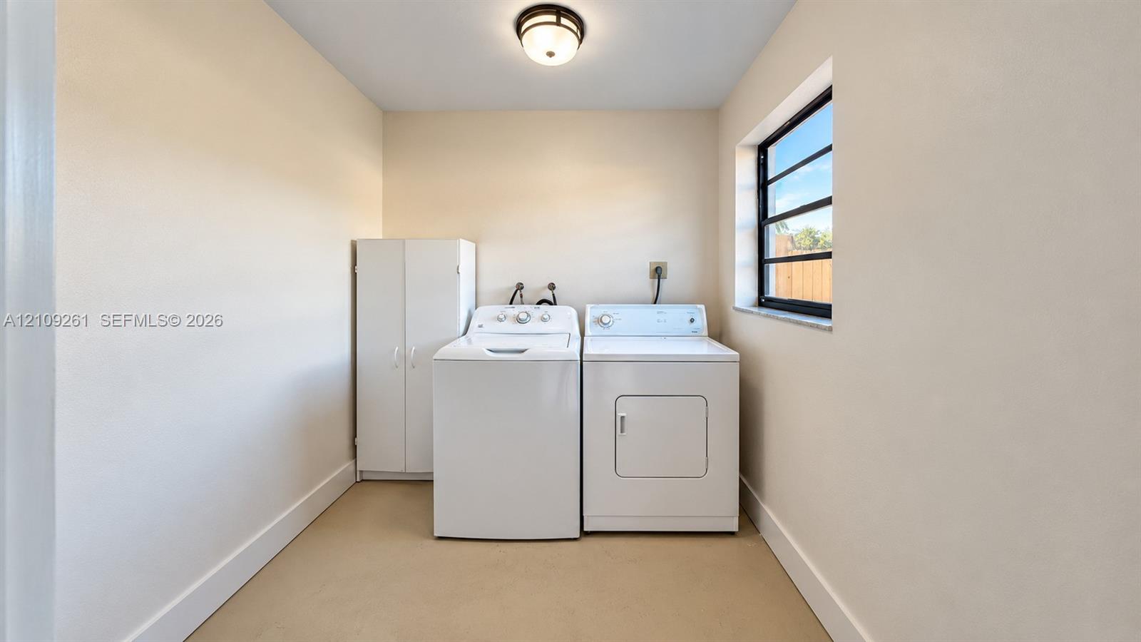 Laundry area featuring a built-in white storage cabinet, a window with multi-pane glazing, and a flush-mount ceiling light fixture