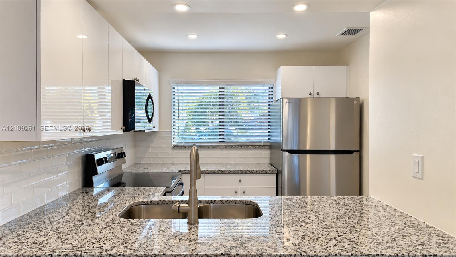Kitchen featuring white cabinetry, stone-finish countertops, stainless steel appliances, a double-basin undermount sink, and recessed ceiling lighting