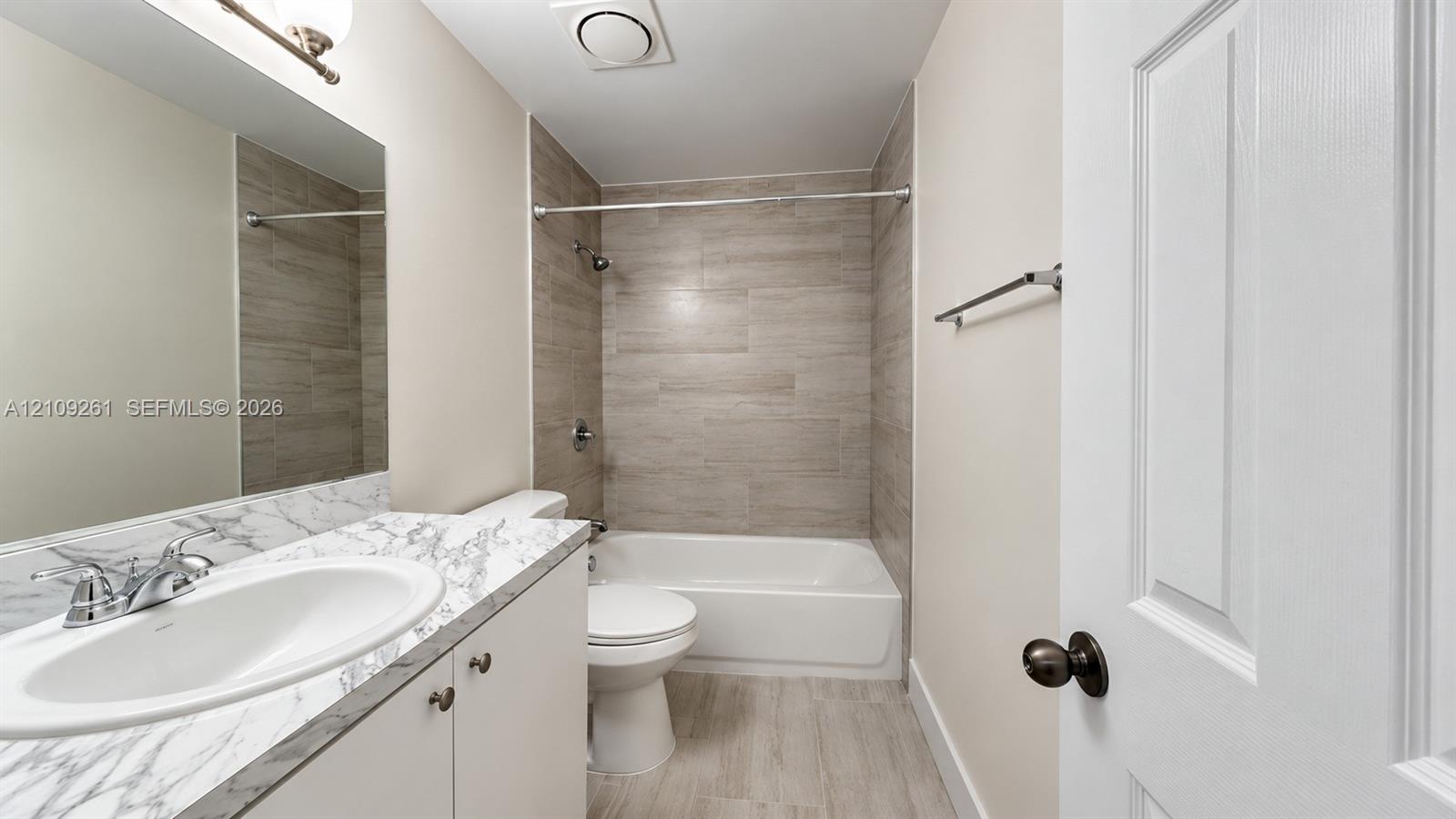 Full bathroom featuring a vanity with a stone-patterned countertop, an integrated sink, a bathtub with a tiled surround, and wood-finish tile flooring