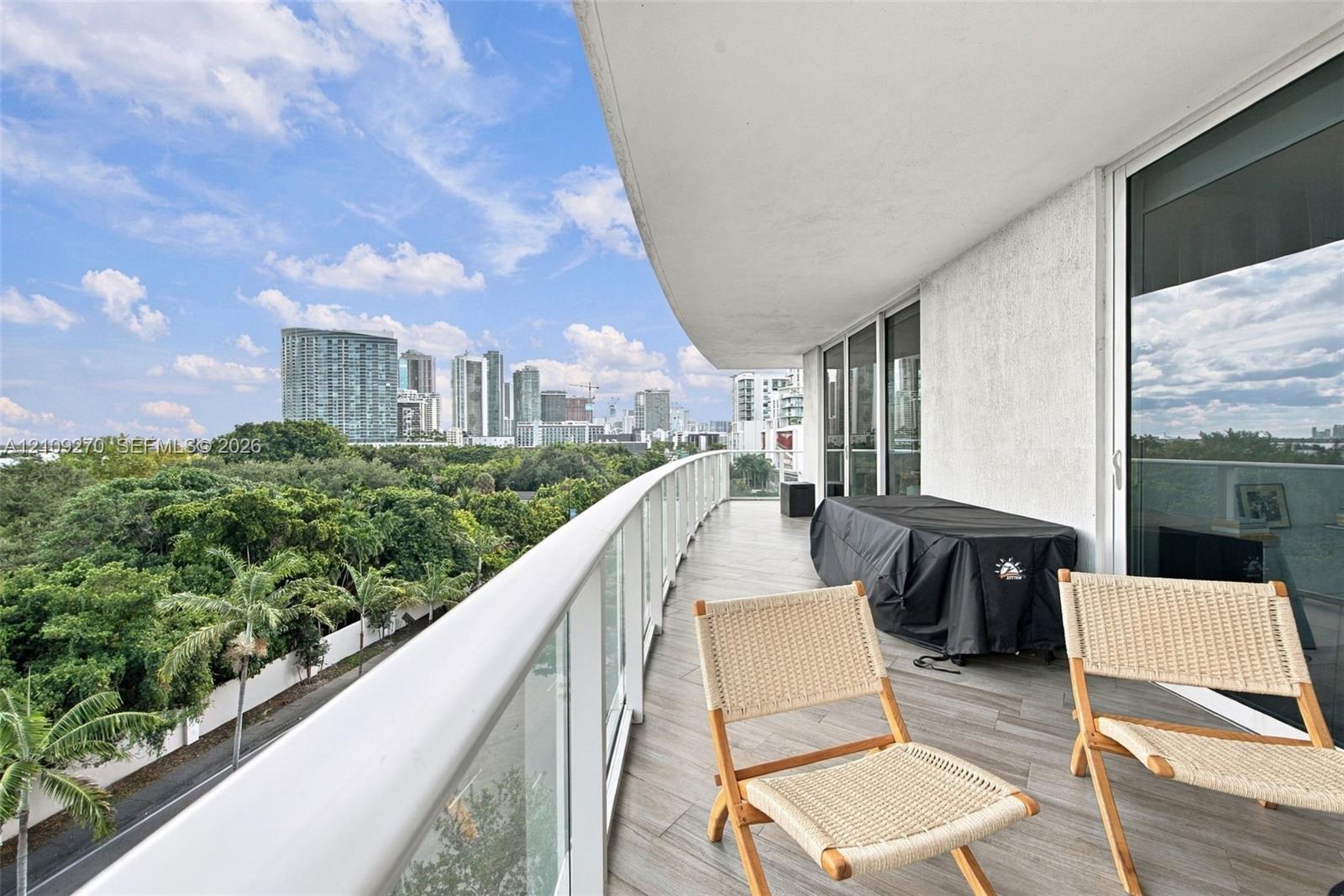 Spacious covered balcony featuring wood-finish tile flooring, glass panel railings, and metal structural supports