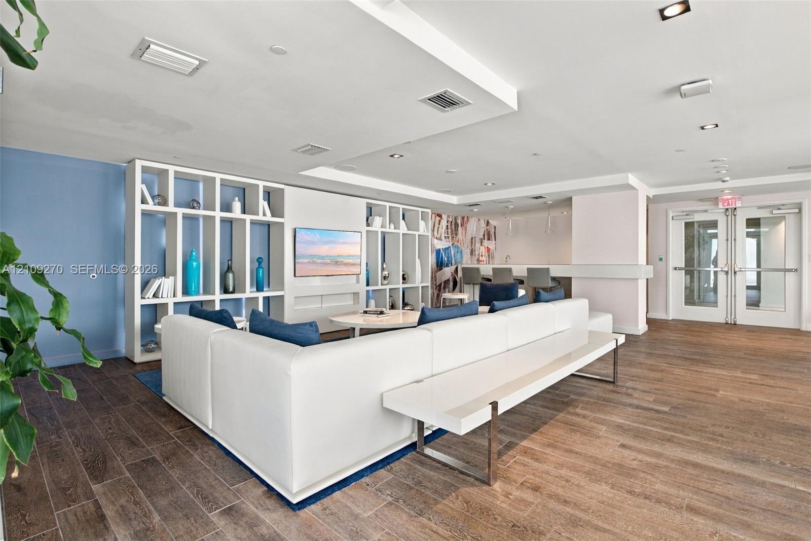 Open-concept common area featuring wood-finish flooring, floor-to-ceiling built-in shelving, recessed ceiling lighting, and double-door glass entry