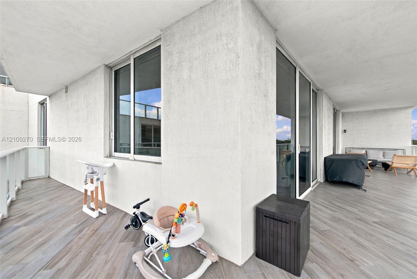 Covered balcony featuring wood-finish flooring, sliding glass door access, and white stucco walls