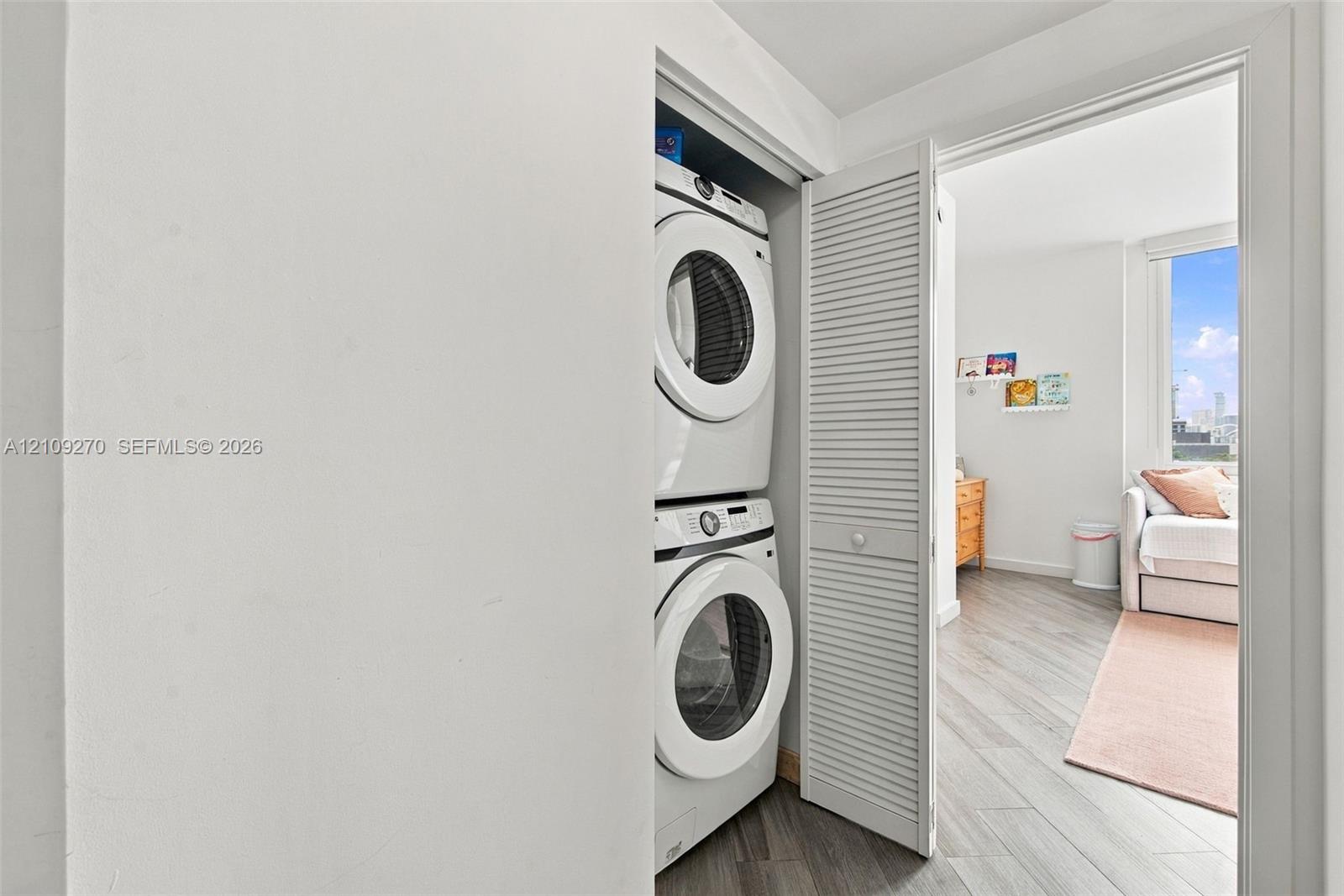 Laundry closet featuring a stackable washer and dryer unit enclosed by white louvered bi-fold doors
