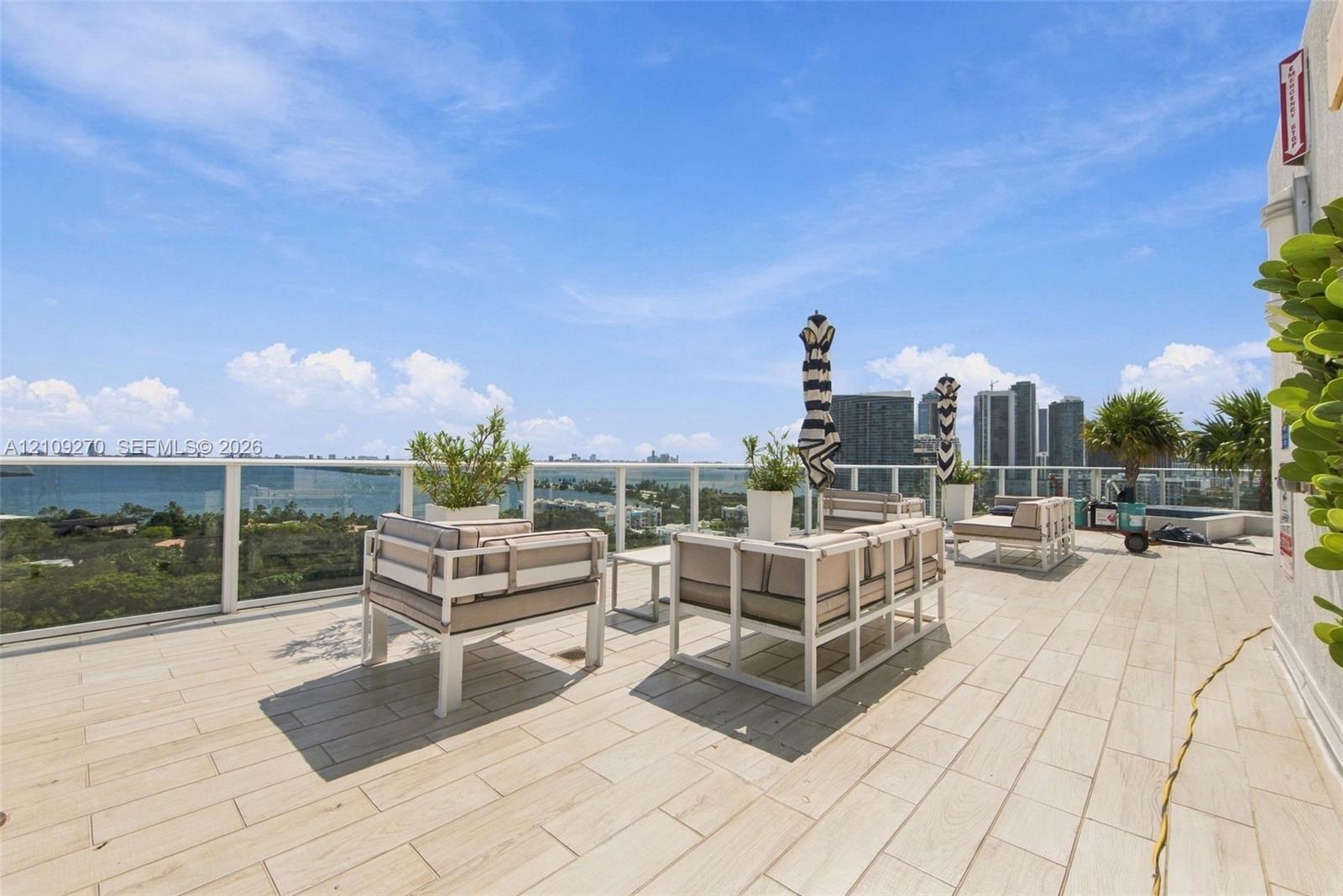Expansive outdoor terrace featuring light-toned tile flooring, a glass panel railing, and a cityscape and water backdrop