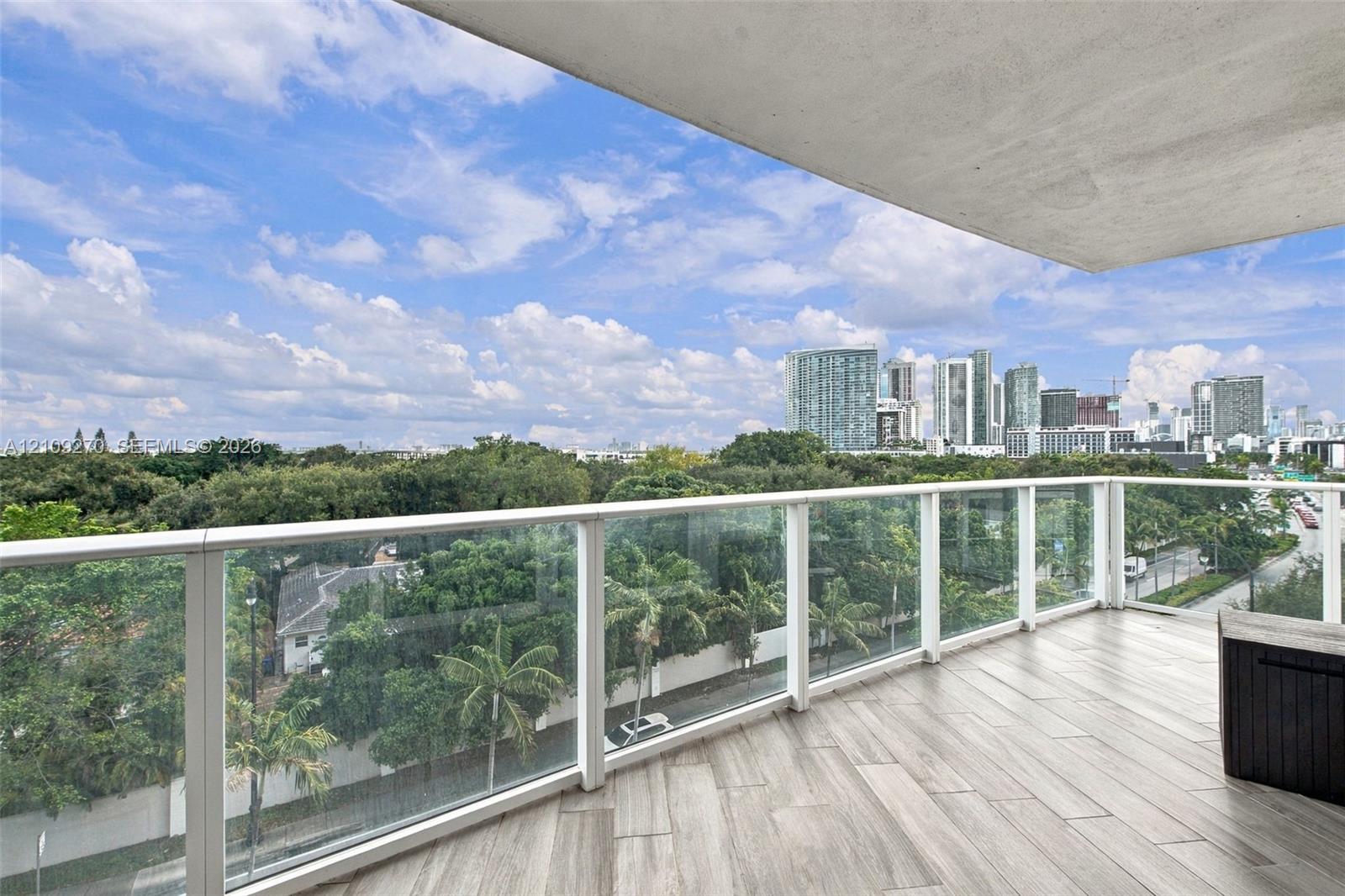 Covered balcony featuring wood-finish flooring, glass panel railings, and urban skyline scenery