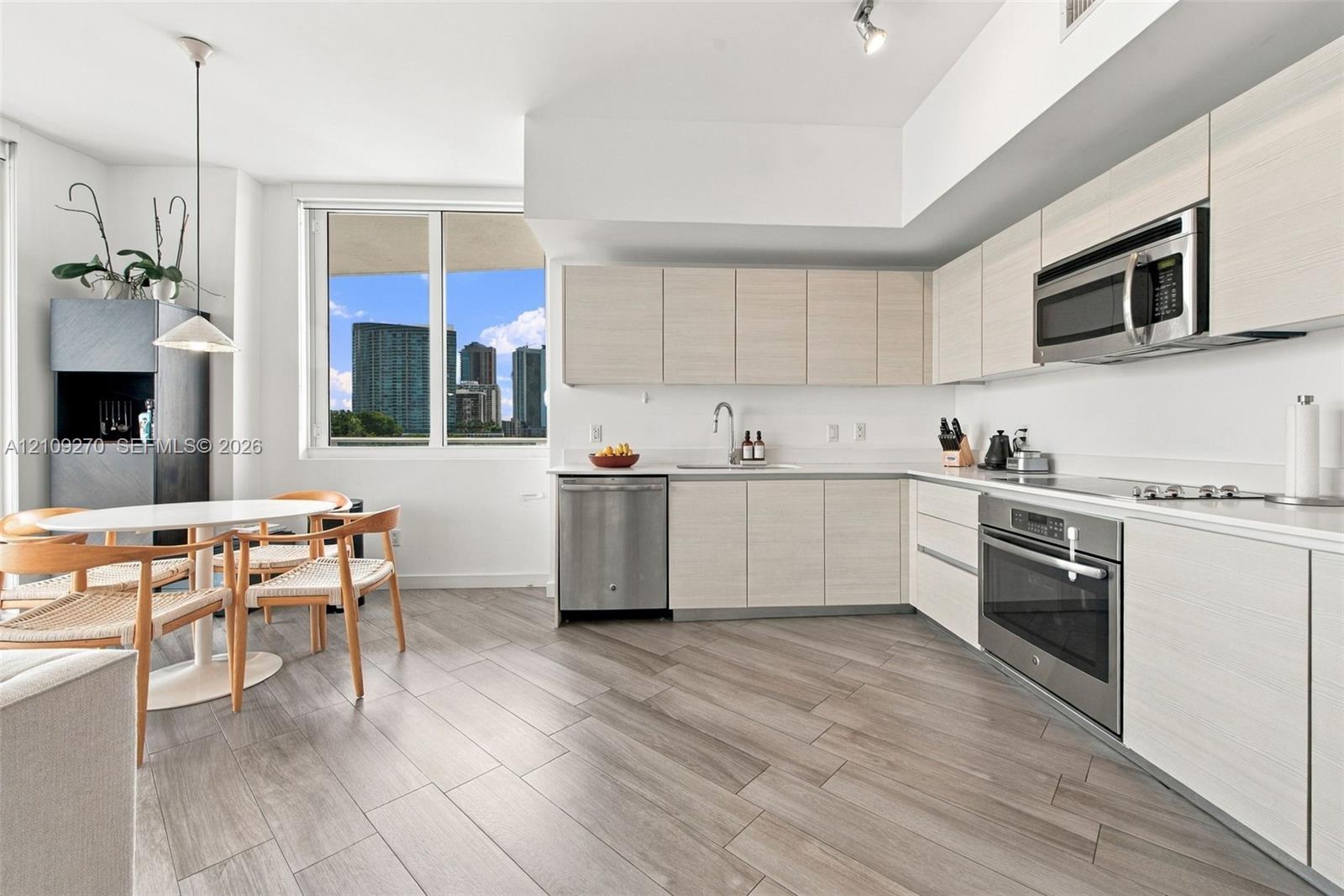 Kitchen featuring light-toned cabinetry, stainless steel appliances, wood-finish flooring, and expansive windows