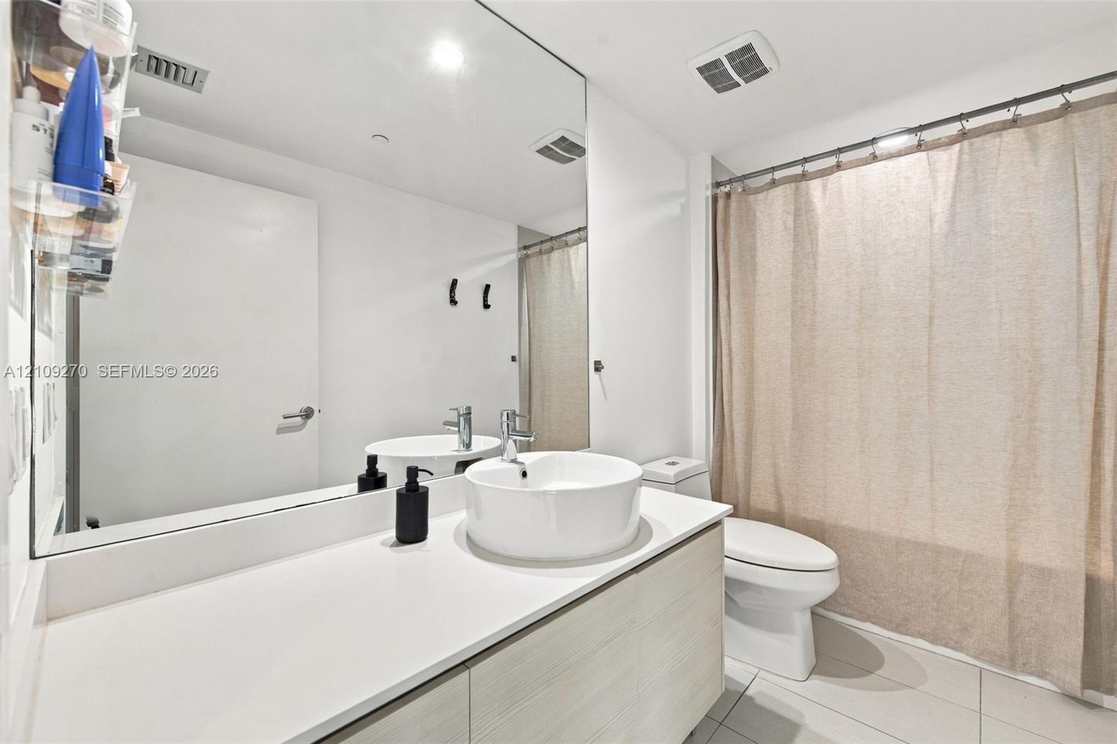Modern floating vanity with a light wood-finish cabinet, rectangular surface-mounted sink, and wide-format wall mirror featuring a polished chrome faucet