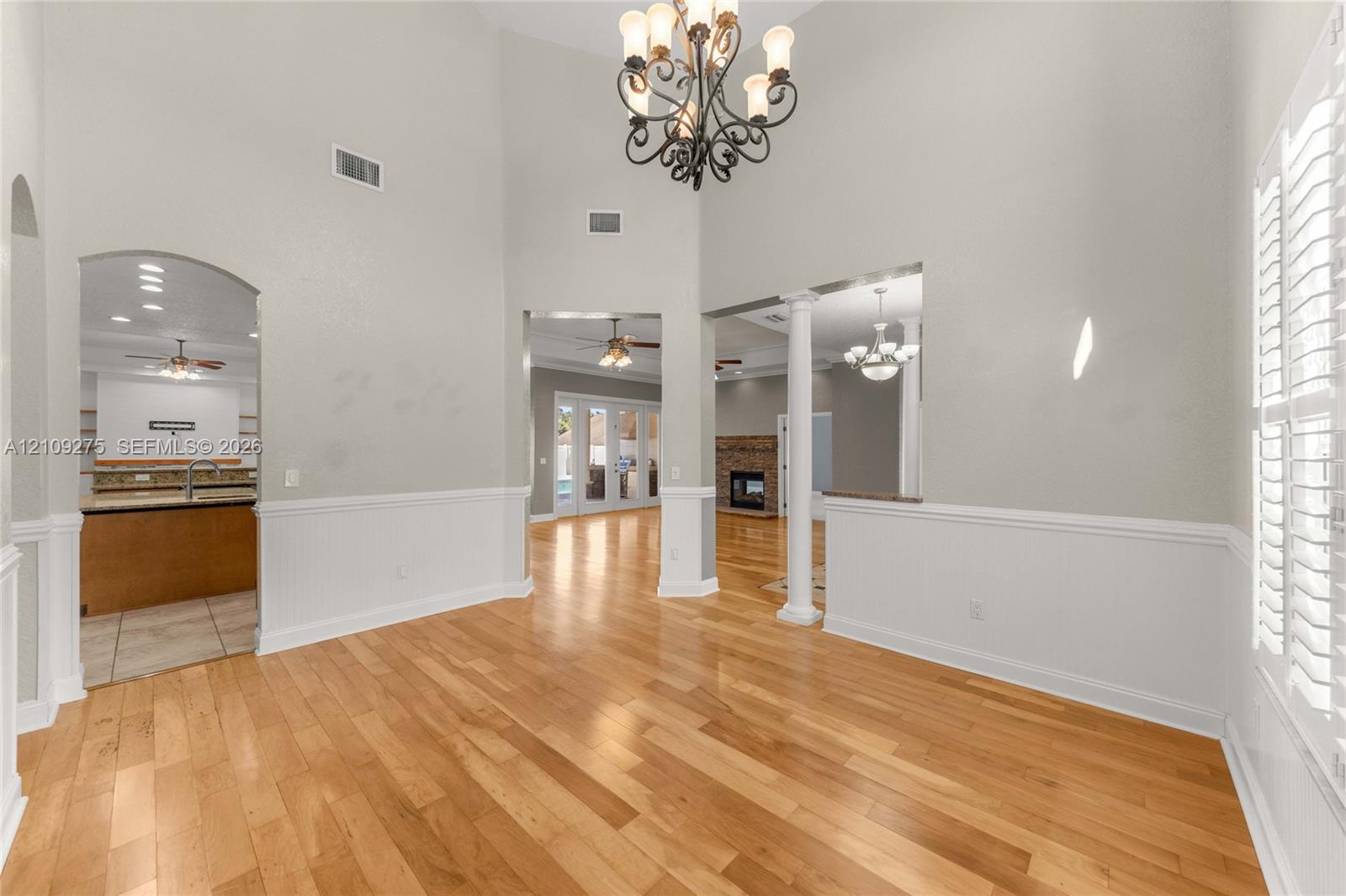 Vaulted ceilings featuring an ornate wrought-iron chandelier, wood-finish flooring, architectural columns, wainscoting, and plantation shutters