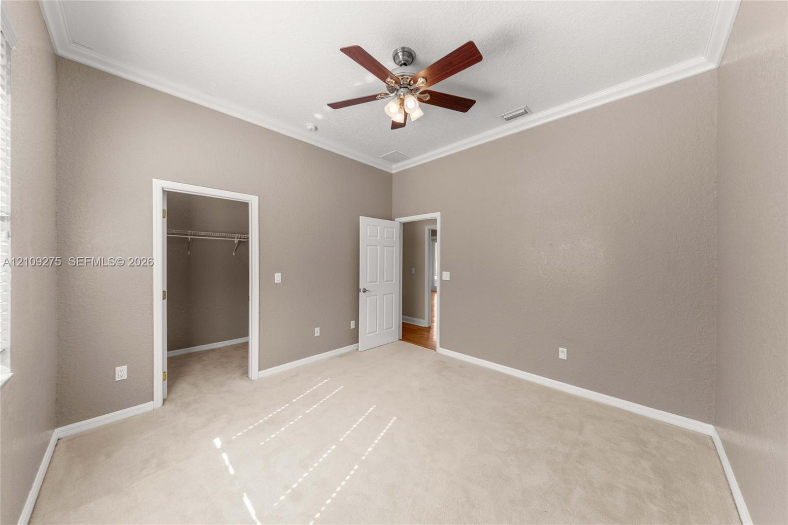 High ceilings with crown molding, neutral carpeting, ceiling fan with integrated light fixture, and interior walk-in closet with built-in shelving